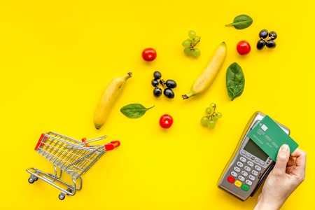 Making purchase products online with card machine, fruits and mini trolley on office desk background top view.の写真素材