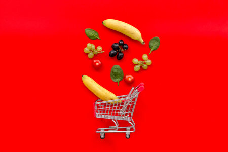 Mobile shopping in online shop. Shopping cart with fruits, vegetables and products on red background...