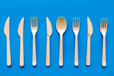Go green. Plastic flatware for eco and Earth protection concept on blue background top view