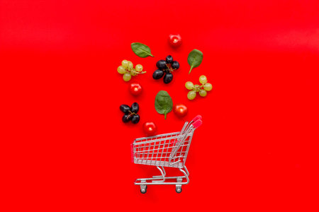 Buying products online with fruits and mini trolley on red desk background top view space for text