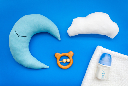 Baby care concept with moon pillow, clouds, feeding bottle and toy for sleep of newborn on blue background top viewの写真素材