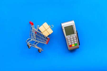 buying products with keyboard, card machine and mini trolley on blue background top view