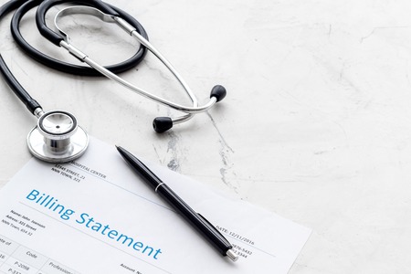 Medical treatment bill and phonendoscope on white desk backgroundの写真素材