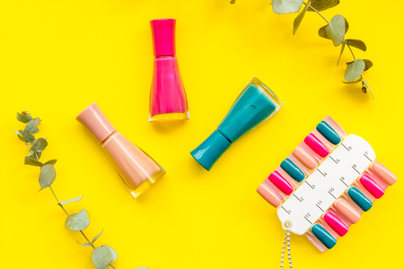 Nail bar desk with nail artist instruments. Decorative cosmetics set with flower, nail polish and palette for manicure on yellow work desk background top viewの写真素材