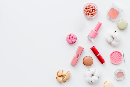 Beauty blogger work. Make-up artist desk with flowers, powder, lipstick, blusher, nail polish, decorative cosmetics and macaroon cookies on white background top view mockupの写真素材