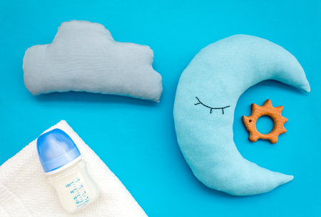 Put baby into bed. Baby care concept with moon pillow, clouds, feeding bottle and toy for sleep of newborn on blue background top viewの写真素材