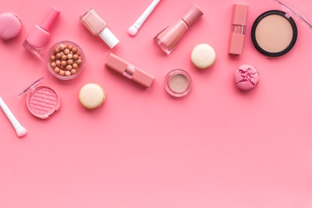 Blusher, powder, lipstick, nail polish. Decorative cosmetics for make-up with macaroon cookies on pink tabletop background mockupの写真素材