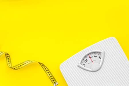 Diet. Bathroom scales and measuring tape for weight loss concept on yellow background top view mock upの写真素材