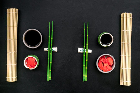 Oriental table set up. Japanese food cooking set with soy sauce, ginger, bamboo sticks for sushi or maki on black background top viewの写真素材