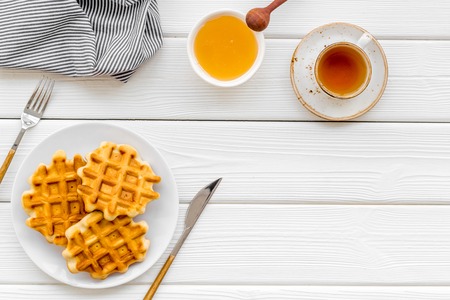 Breakfast with Belgian waffles with honey, tea, knife, fork and spoon on white wooden background top view mockupの写真素材