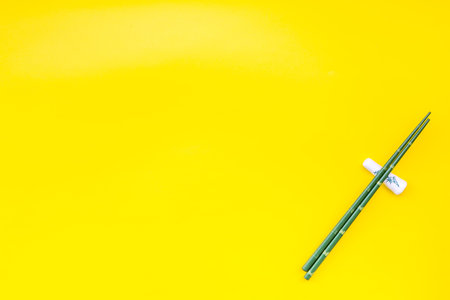 Table set up. Asian cuisine set with bamboo sticks for sushi and maki on yellow background top view mock upの写真素材
