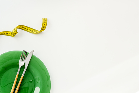 Medical starvation concept. Empty plate with fork and knife near measuring tape on white background top viewの写真素材