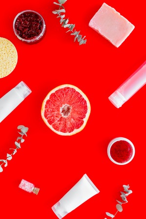 Scrubs and creams for homemade spa. Organic cosmetics with herbs and grapefruit on red background top viewの写真素材