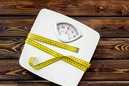 Proper nutrition. Medical starvation. Slim concept with scale and measuring tape on wooden...