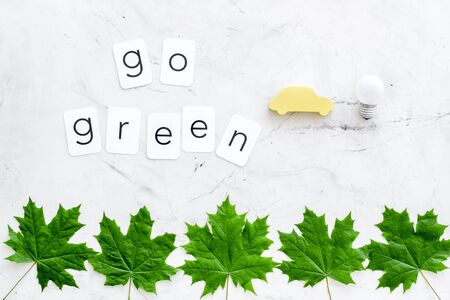 Go green concept with maple leaves, car and lamp on white marble background top viewの写真素材