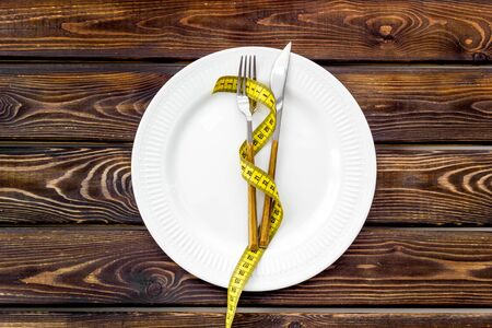Diet concept with plate, flatware and measuring tape for weight loss on wooden background top viewの写真素材