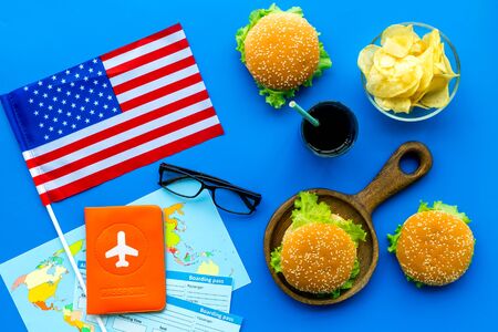 Gastronomical tourism concept with american flag, passport, tickets, map and food symbols, burgers, chips, coke on blue background top viewの写真素材