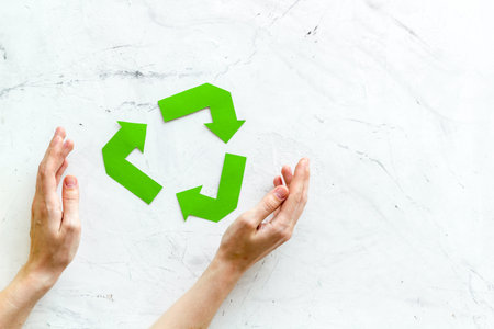 Recycling symbol in hands on white marble background top view