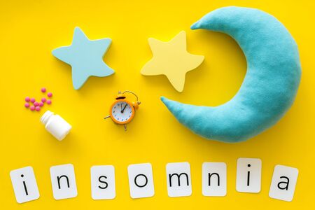 Try to sleep. Insomnia concept with moon, stars toy, alarm clock and pills on yellow background top viewの写真素材