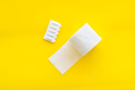 Disease of colon. Proctology concept with toilet paper roll and rectal suppository on yellow background top viewの写真素材