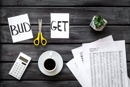 Business budget. Sciccors and paper with word budget, coffee and plan for budget reducing on wooden background top view
