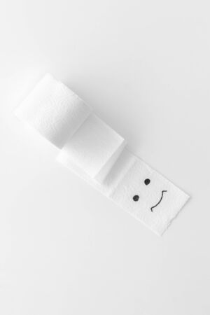 Disease of colon. Proctology concept with toilet paper roll and painted face on white background top viewの写真素材