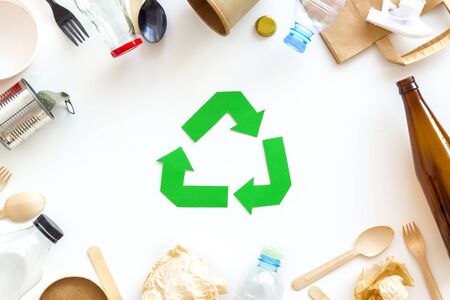 Ecology concept. Green recycling sign with waste materials, paper bag and cup, plastic bottles, flatware on white background top viewの写真素材