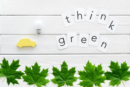 Ecology friendly. Think green text with car toy, lamp, green maple leaves on white wooden background top viewの写真素材