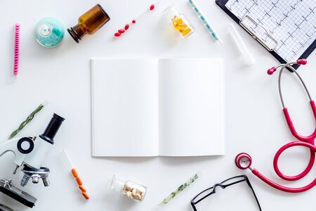 Desk of doctor in laboratory. Medical research concept with notebook, microscope, stethoscope, cardiogram, test tube frame on white background top view mockupの写真素材