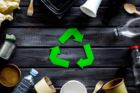 Ecology concept. Green recycling sign with waste materials, paper cup, plastic container, bottles, flatware on wooden background top viewの写真素材
