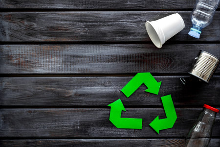 Green recycling symbol with cup, plastic bottle, can for ecology on wooden background top view...