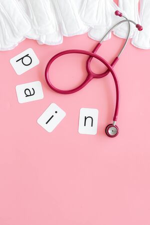 Gynaecologist. Woman hygiene and menstrual period concept with sanitary pads, stethoscope and pain word on pink background top view mockupの写真素材