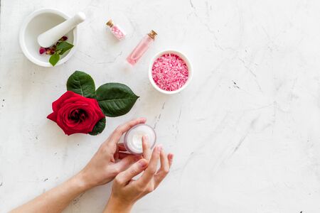Natural organic cosmetics with rose extract in hands. Cream, lotion, spa salt and flower on white marble background top view copyspaceの写真素材