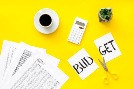 Business and accountant concept with coffee, scissors, cut budget copy and calculator on yellow office work desk background top viewの写真素材