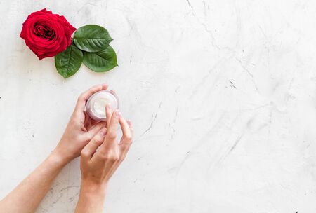 Cosmetic spa set with rose flowers and cream for body in hands on white marble desk background top view mockupの写真素材