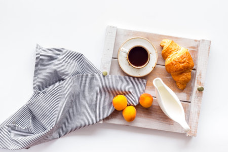 Breakfast in bed with croissant, coffee in cup with milk on tray on white background top viewの写真素材