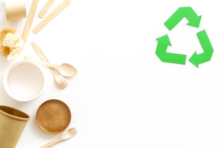 Green paper recycling sign with waste materials paper, cup, wooden flatware, spoon, fork on white background top view space for textの写真素材
