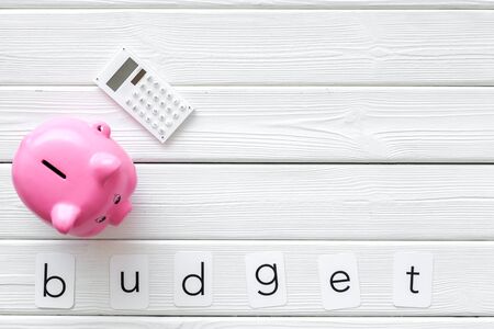 Business concept with budget word, piggy bank and calculator on white wooden office desk background top view space for textの写真素材