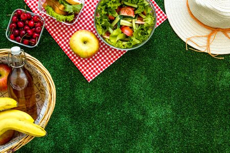 Basket with food. Picnic in summer with products, sandwich, salad, fruits, drink, apples, cherry and hat on green grass texture background top view mockupの写真素材