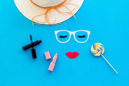 Visagiste or stylist job. Decorative cosmetic for make up with face model, lollipop, mascara, hat and lipstick on blue background top viewの写真素材