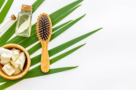 Bottle with jojoba, argan or coconut oil, hair brush for styling on plant on white background top view mock-upの写真素材