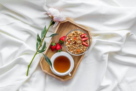 Homemade breakfast on the tray with granola, tea and fruit on white bed sheet background top viewの写真素材
