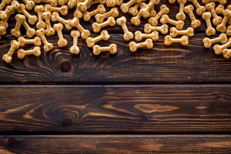 Pet care. Dry dog food in shape of bone on wooden background top view copy space