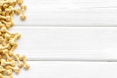 Dry pet food in shape of bone on white wooden background top view copyspace