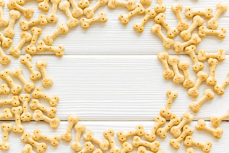 Pet care. Dry dog food in shape of bone frame on white wooden background top view copy space