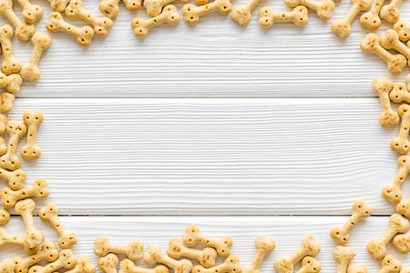 Pet care. Dry puppy food in shape of bone frame on white wooden background top view copyspace