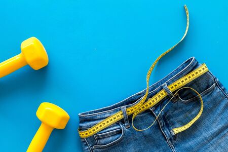 Diet, fitness and body shape. Trousers with bars and measuring tape for weight loss and sport concept on blue background top view space for textの写真素材
