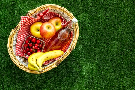 Basket with food. Picnic in summer with products, apples, banana, cherry, drinks and tablecloth on green grass texture background top view space for textの写真素材