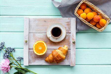 Breakfast on the tray with croissant, coffee and fruit on mint green wooden background top viewの写真素材