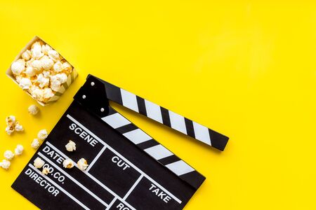 Movie premiere concept. Watch film in cinema with popcorn, video tape and clapperboard on yellow background top view mockupの写真素材
